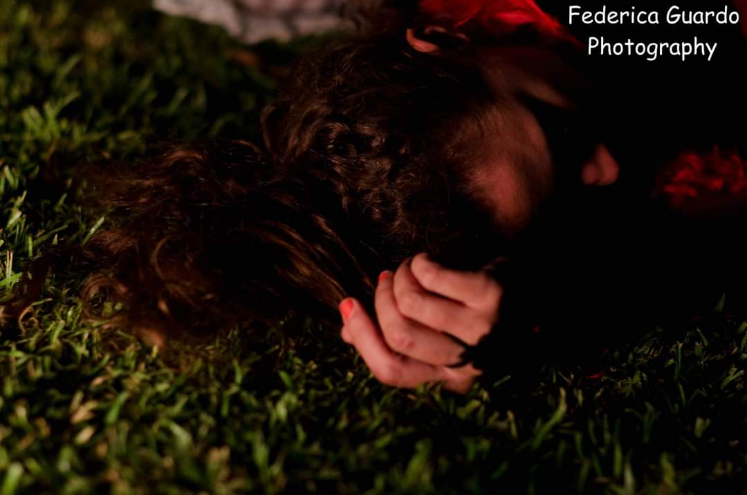 A woman with long, brown hair is shown lying down in grass, with her head in her hands.