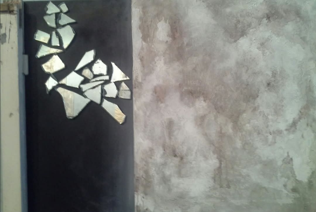 A fragment of broken mirror against a dirty gray wall.