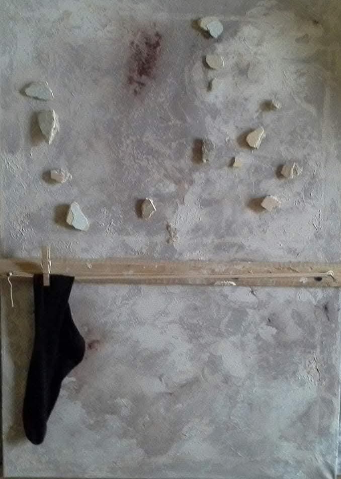 Installazione materica con muro grigio, sassi applicati e calza nera appesa