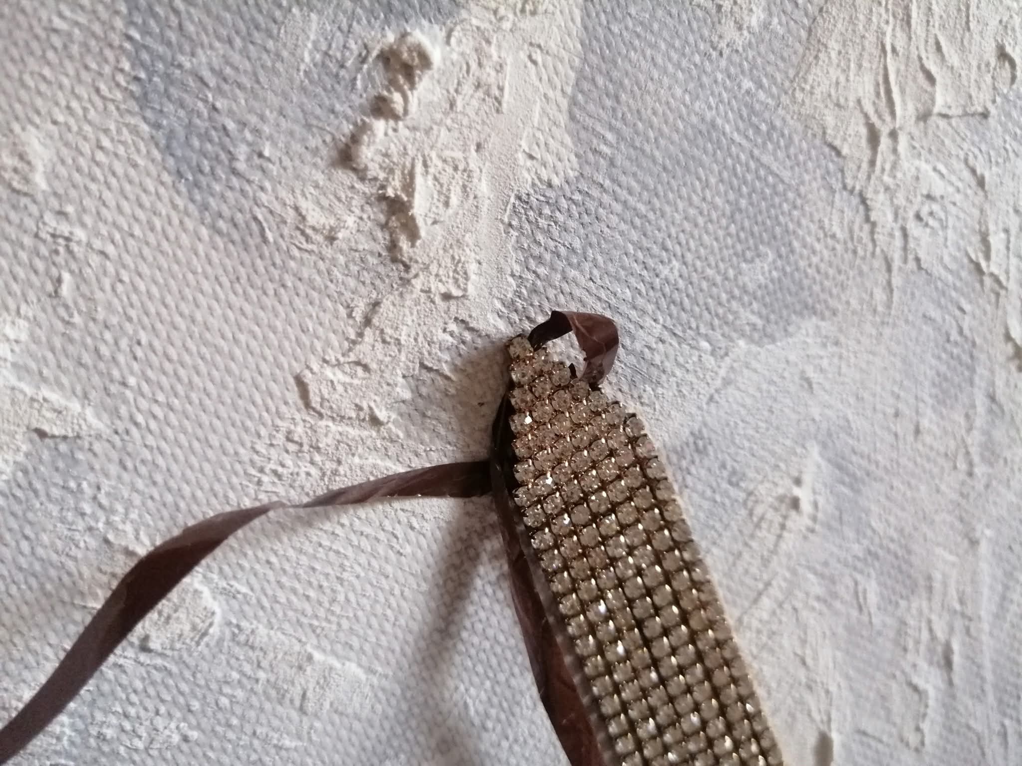 Dettaglio materico con superficie bianca e nastro marrone legato a elemento brillante