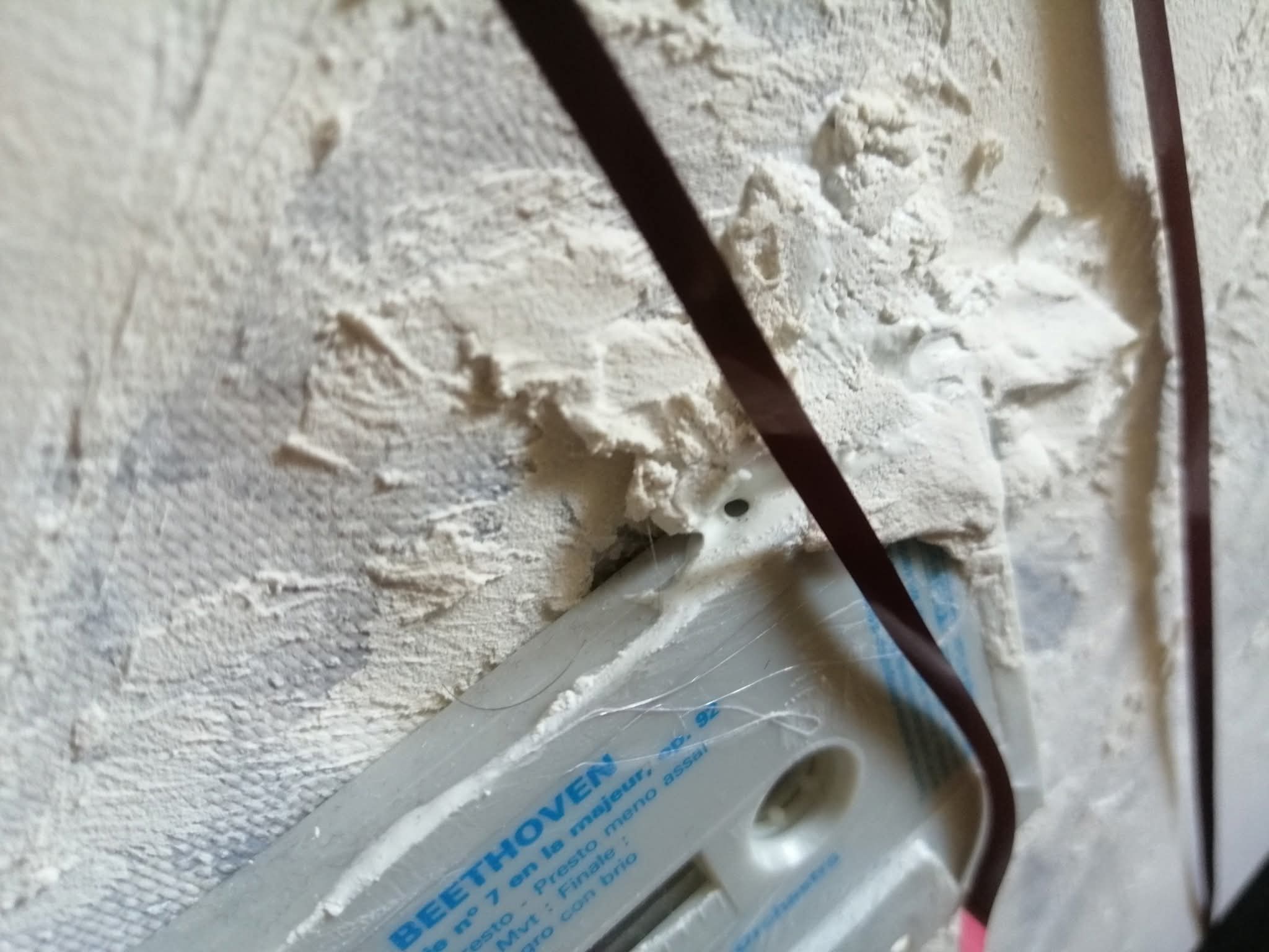 Dettaglio materico con cassetta musicale parzialmente inglobata nella superficie bianca